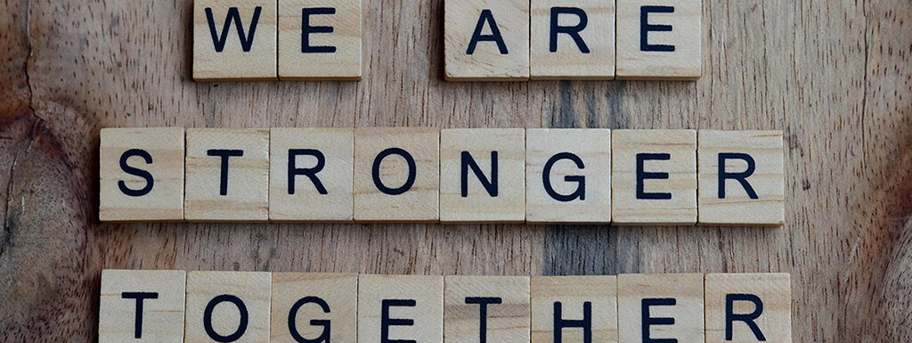 Scabble letters on wood background spelling We Are Stronger Together